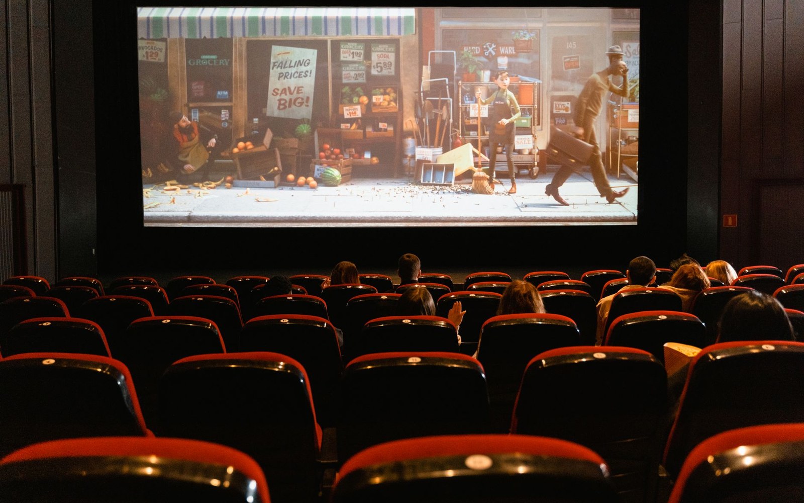 An adult audience seated in a small cinema watching a projected surf film, faces lit by the screen
