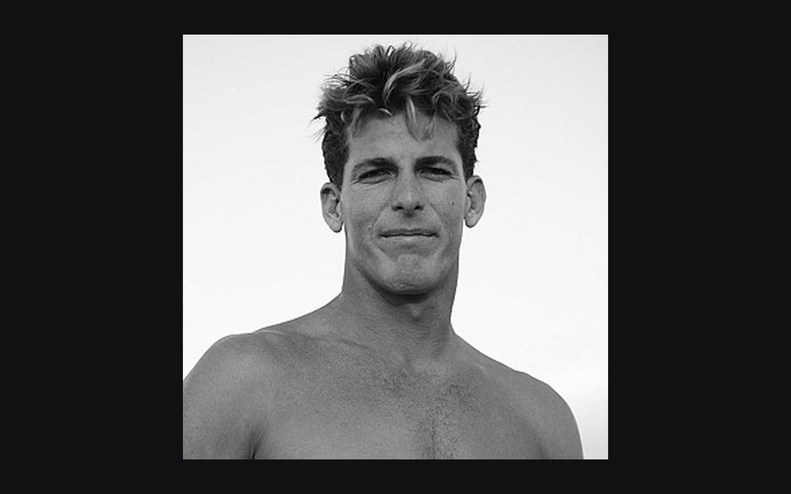 Black and white portrait of a shirtless young man with tousled hair against a plain sky