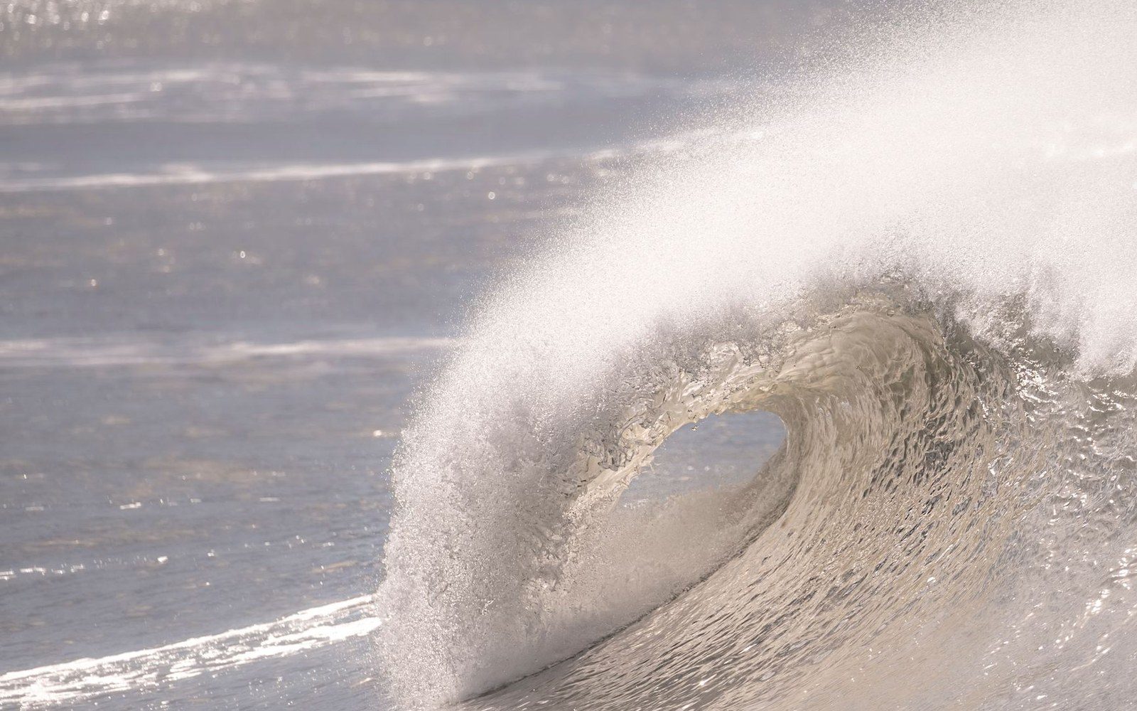 A wave curls into a hollow barrel, spraying fine mist against calmer ocean water