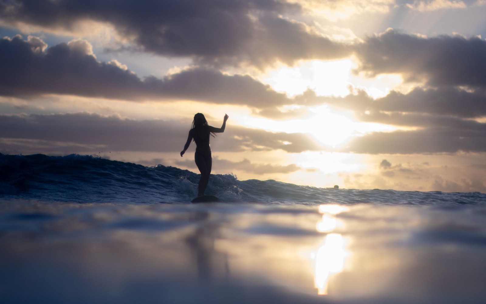 Silhouette of a surfer riding a wave against a cloudy sunset sky
