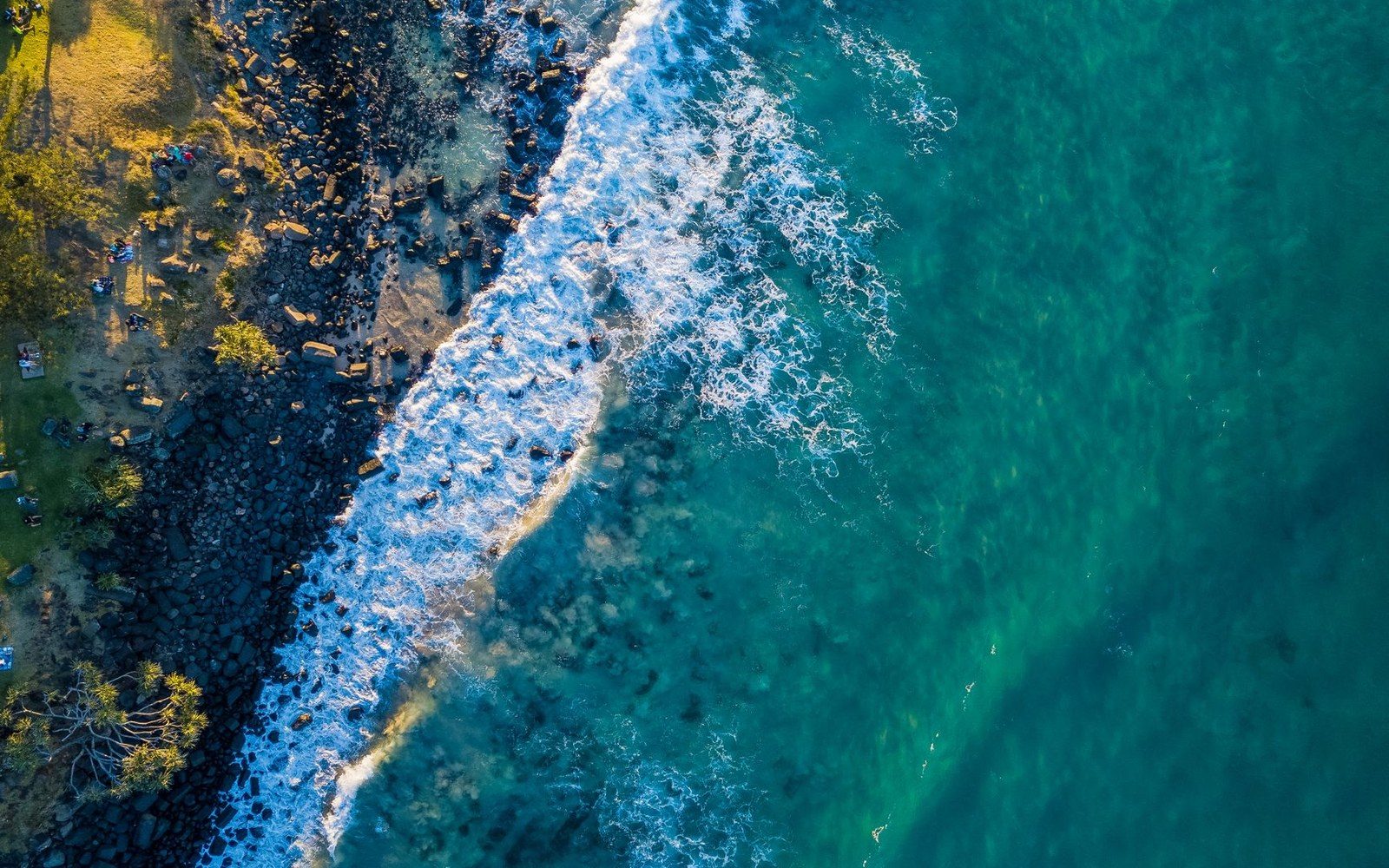 Aerial view of waves breaking over a rocky coastline into turquoise ocean water