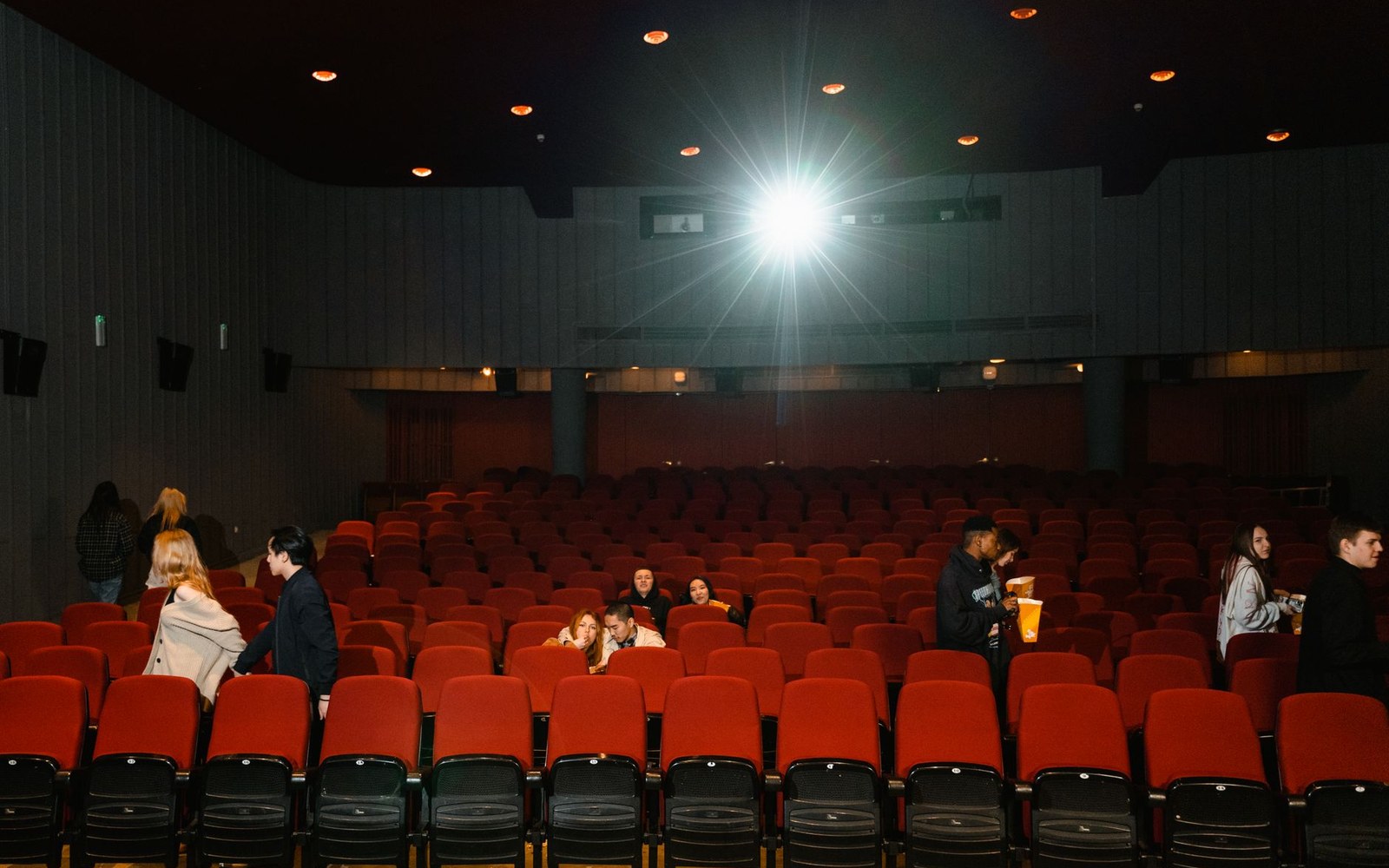 Moviegoers find seats in a mostly empty theater as the projector beams overhead