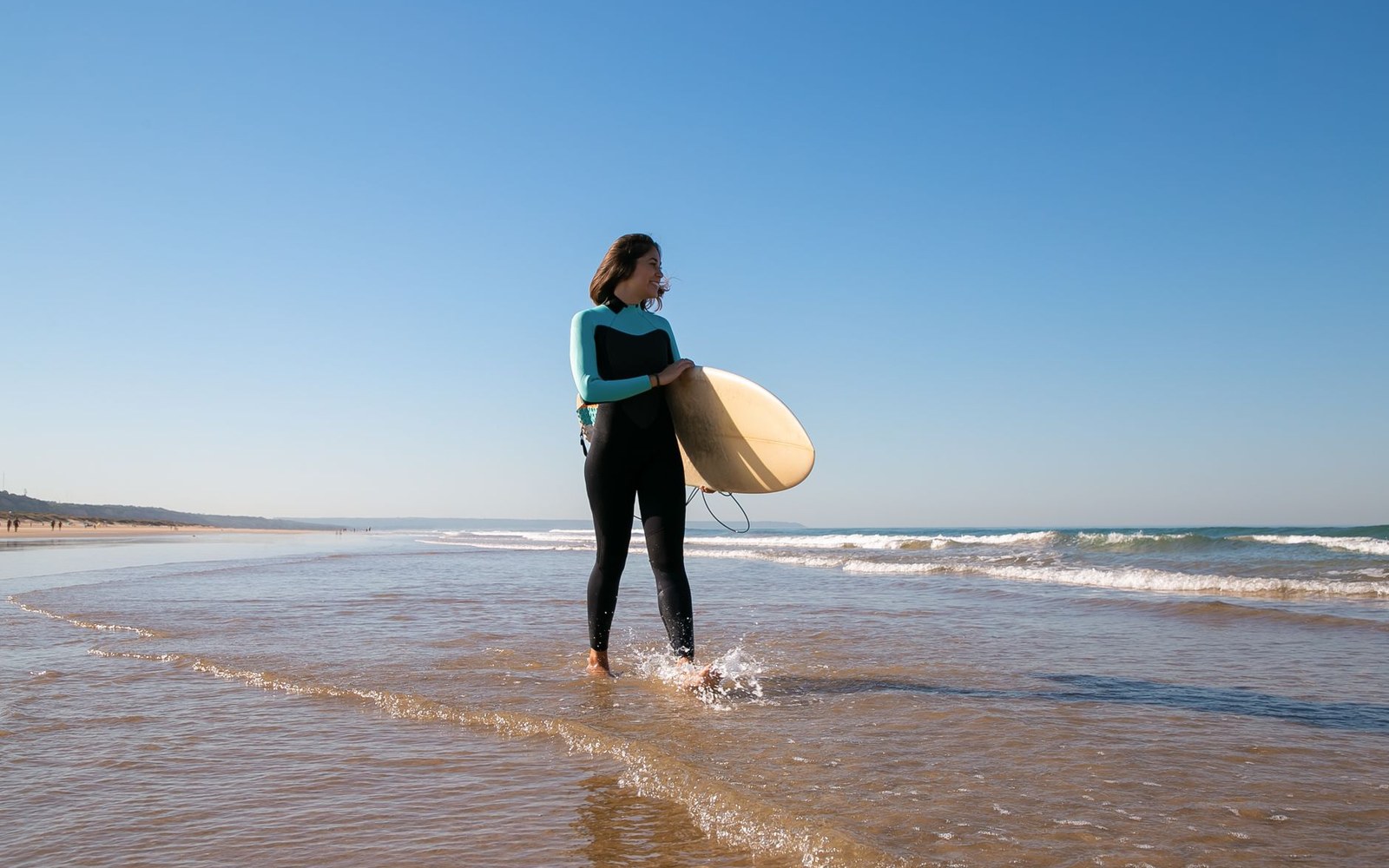 An adult surfer walking toward the water at dawn, board under one arm, Encinitas coastline behind